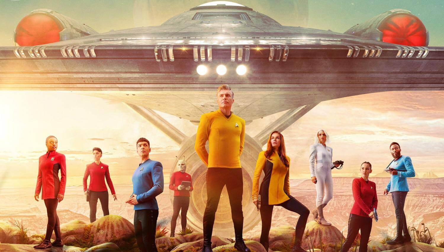 A promotional photo for Star Trek: Strange New Worlds showing the cast standing in front of the Enterprise.