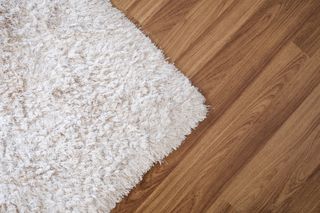 A close-up of a white textured carpet on a deep laminate wood flooring.