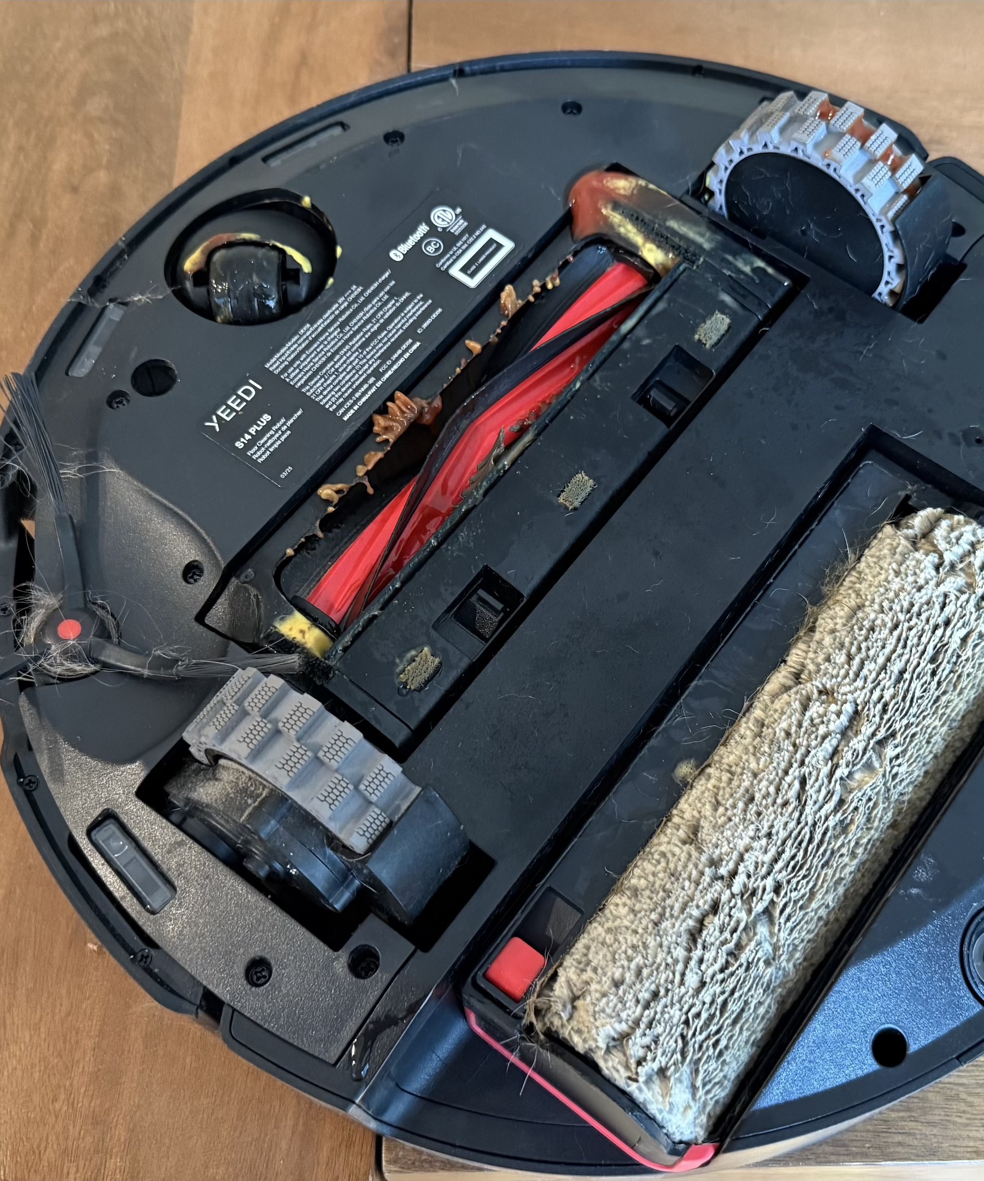 Underside of the Yeedi S14 Plus robot vacuum with ketchup and mustard in wheels and roller, after testing, on wooden floor in James Holland&#039;s home.