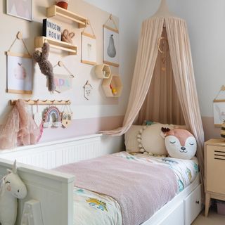 girls bedroom with canopy over bed, shelves with toys and under bed storage