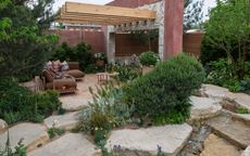 rock garden landscape with pergola, evergreen shrubs and garden furniture