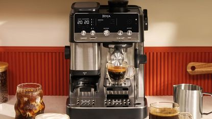 A stainless steel and black espresso machine on a white counter, with a red splashback.