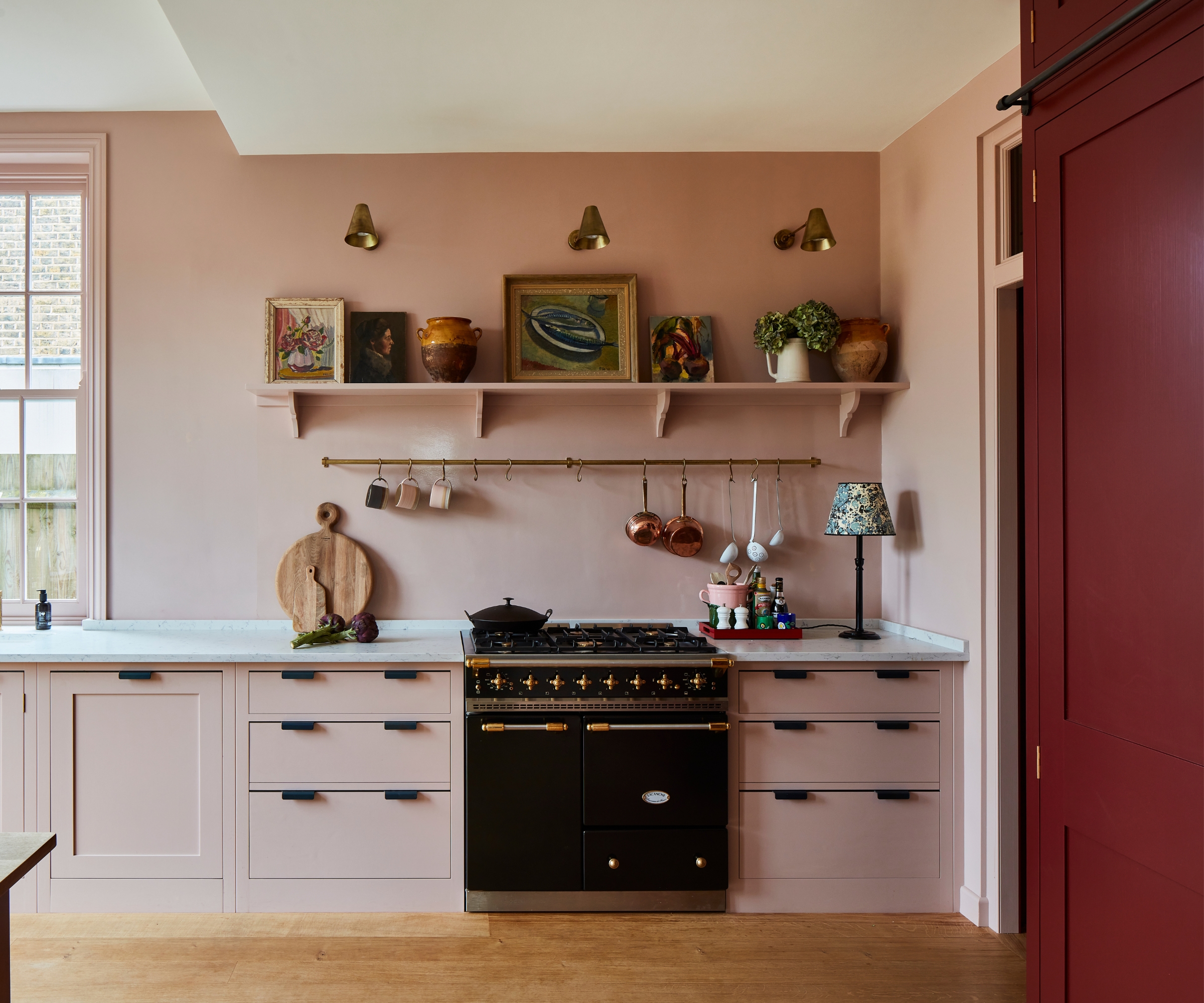 A bright kitchen with pale pink walls and cabinets with burgundy tall cabinets for contrast