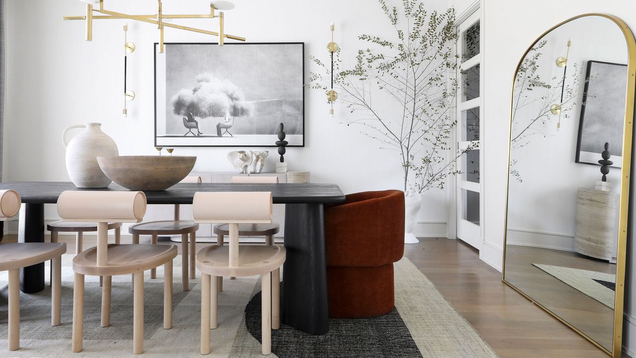 Large arched mirror with gold trim at the top of a black, modern dining room table with wooden accent chairs