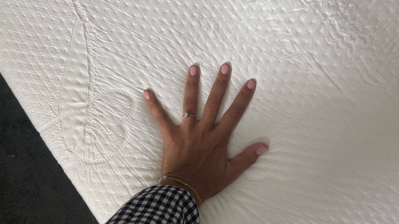 A woman's manicured hand touches the surface of the Puffy Deluxe Mattress Topper cover