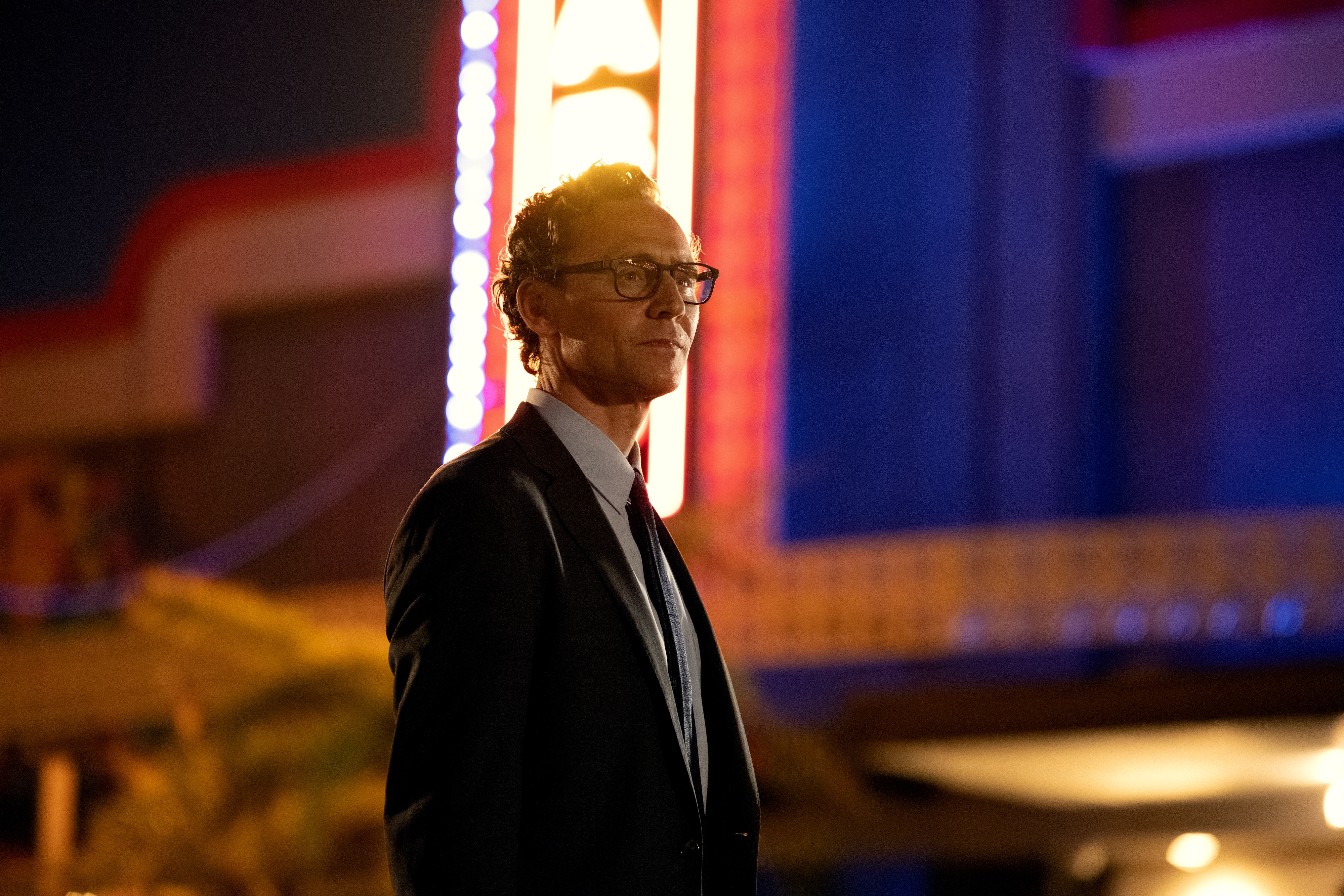 Tom Hiddleston as Chuck Krantz, standing in front of a movie theater marquee, in 'The Life of Chuck.'