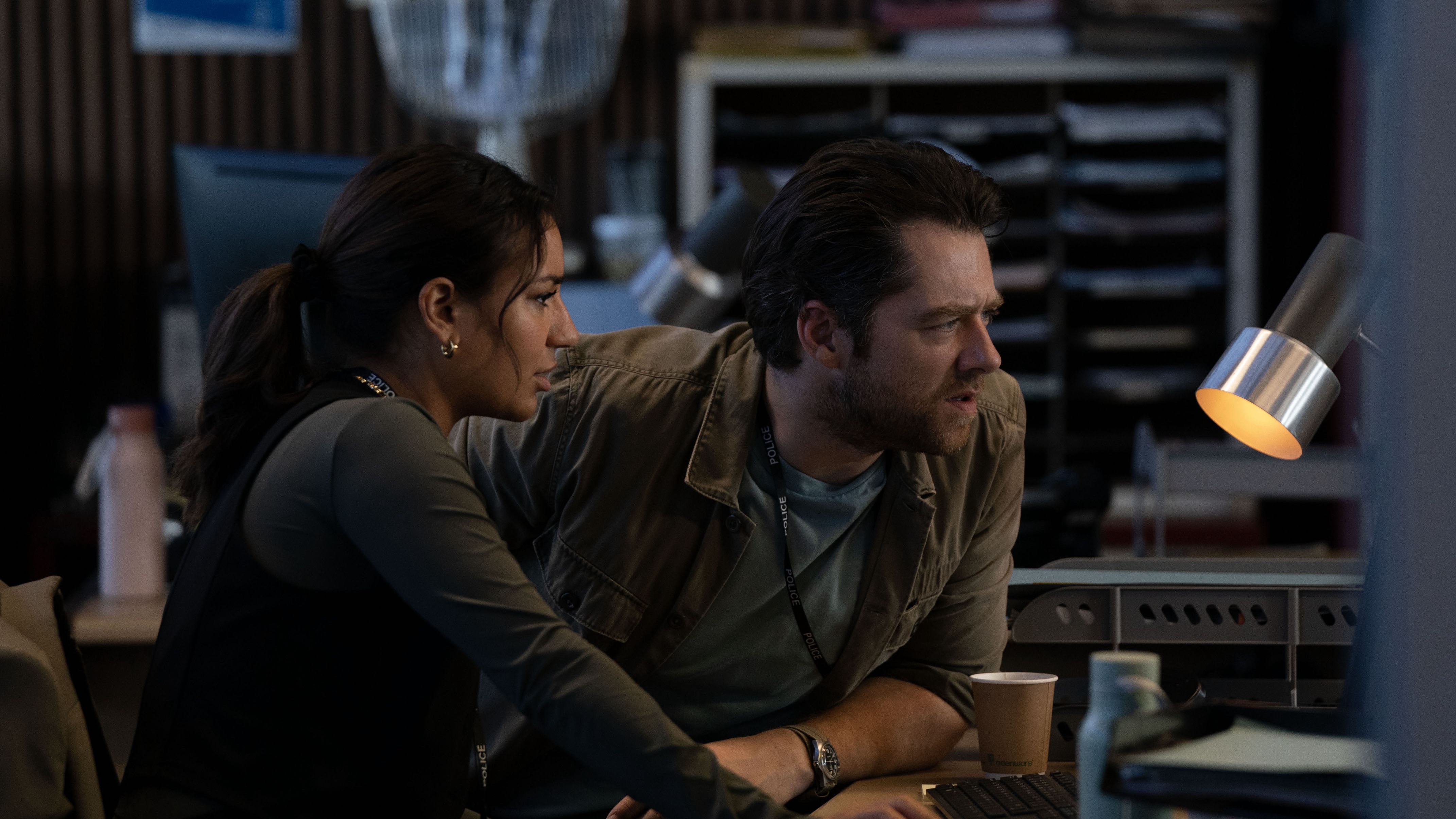 Lucie Shorthouse as DC Siobhan Clarke and Richard Rankin as DS John Rebus sit at a desk looking at a screen in Rebus.