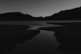 During a solo hike in Wenhai, China, the photographer came across a serene, narrow stream meandering through dark grasslands, flowing towards a vast, still lake in the distance. The image was edited with muted tones and high contrast to evoke the look of a pencil sketch, capturing the solitude and tranquillity of the journey.