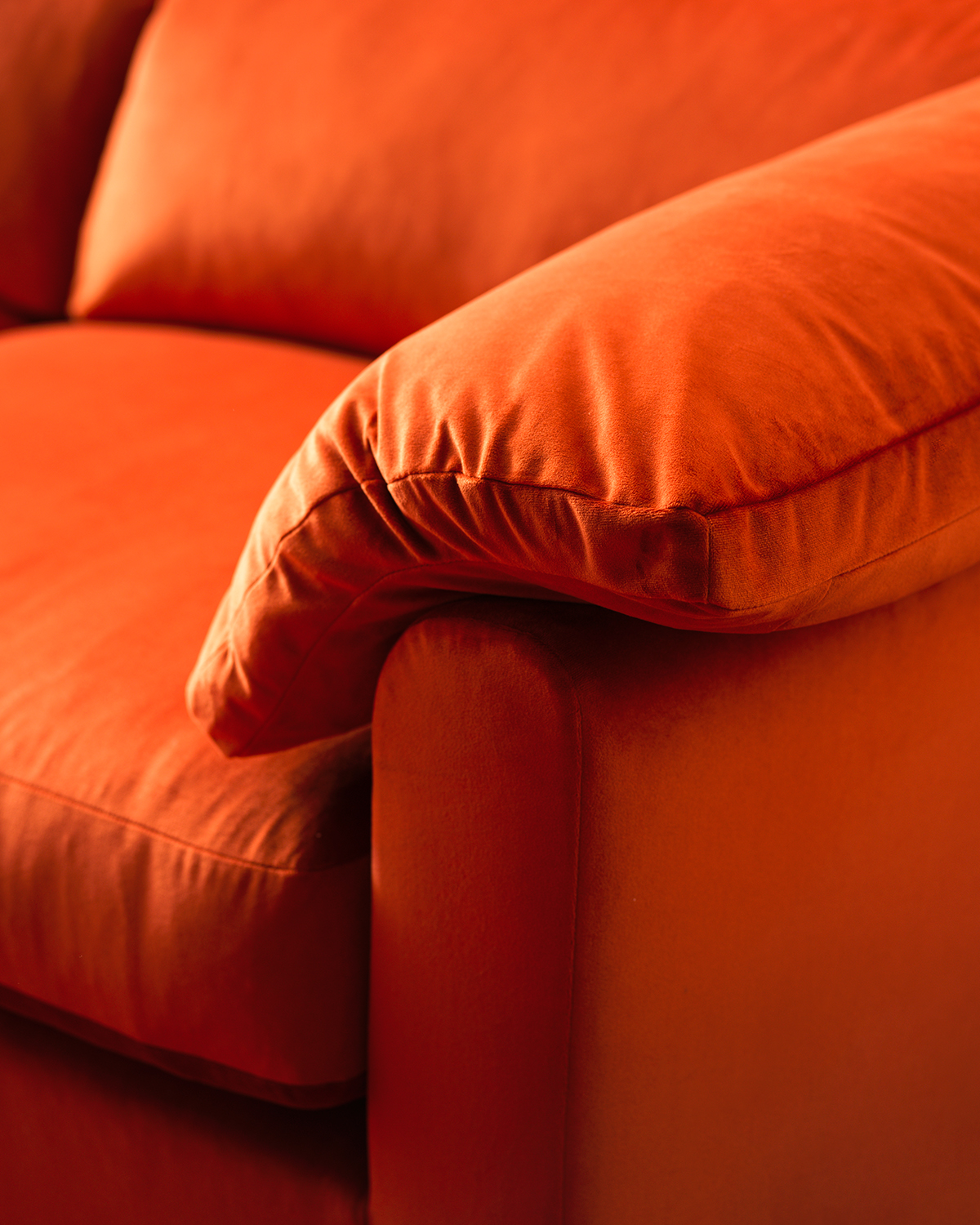 Close-up image of the arm of a velvet, burnt orange sofa