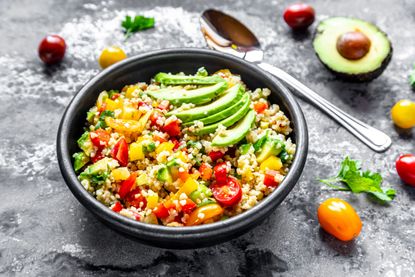 A bowl containing a healthy bulgur wheat salad with tomatoes, slices of avocado and basil.