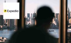 Expedia logo placed over an image of an out of focus shot of a man looking out the window at New York City