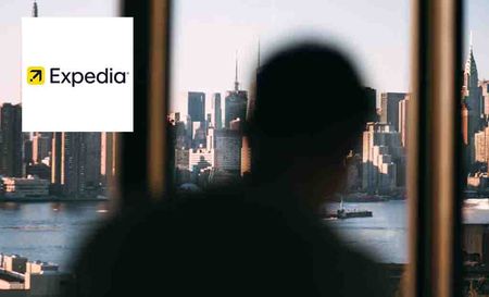 Expedia logo placed over an image of an out of focus shot of a man looking out the window at New York City