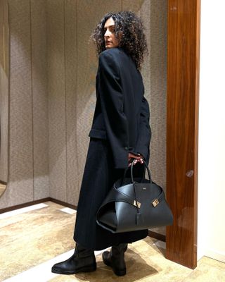 Woman wears black coat, black boots and carries black bag