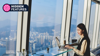 A woman is working on laptop computer while sitting in coffee shop in skyscraper near window with view of metropolitan city.