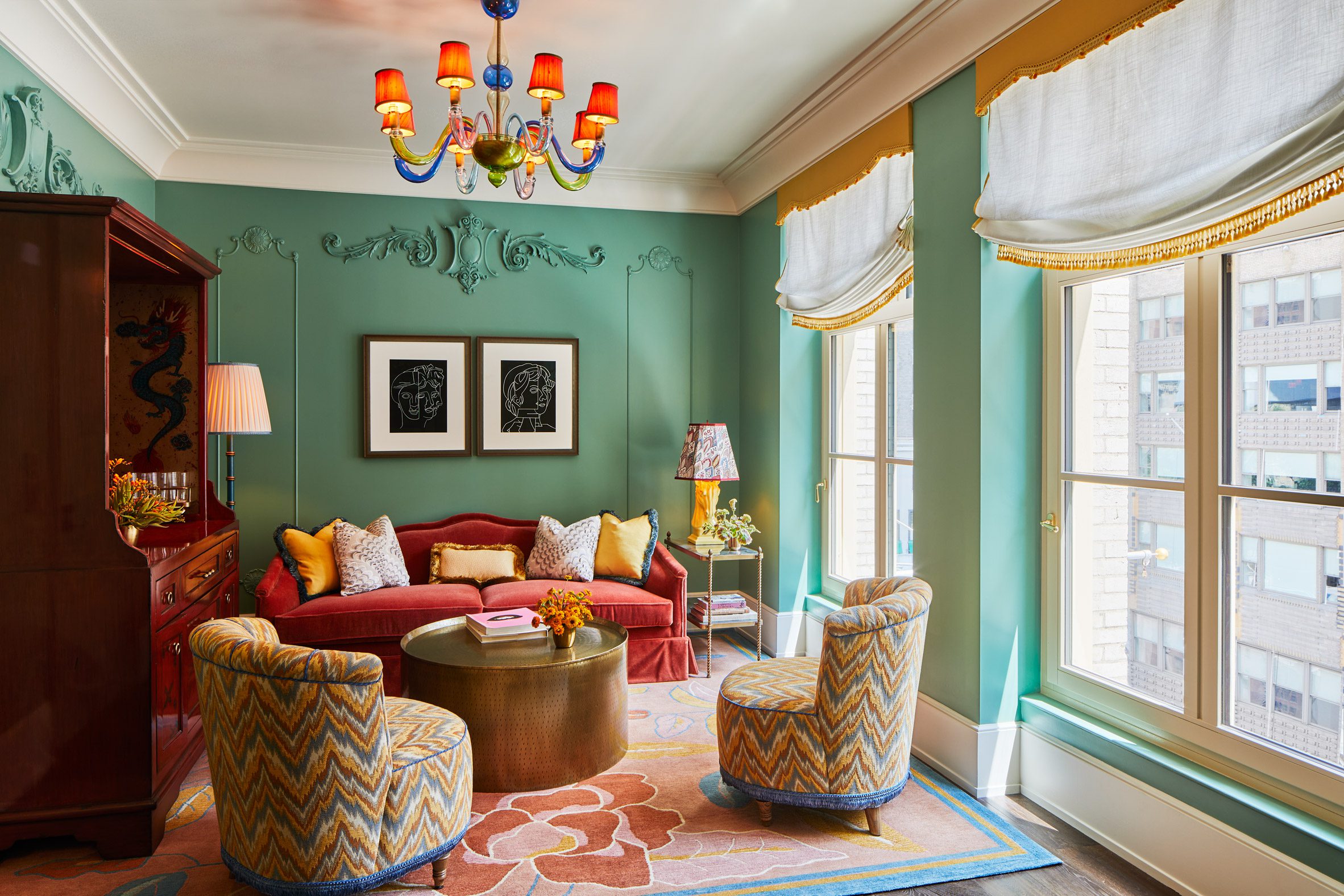 A whimsically decorated, maximalist hotel room is dressed in plush tile, ochre, blue, and terracotta textiles, grand chandeliers and table lamps, and refined upholstery with a nostalgic, retro twist.