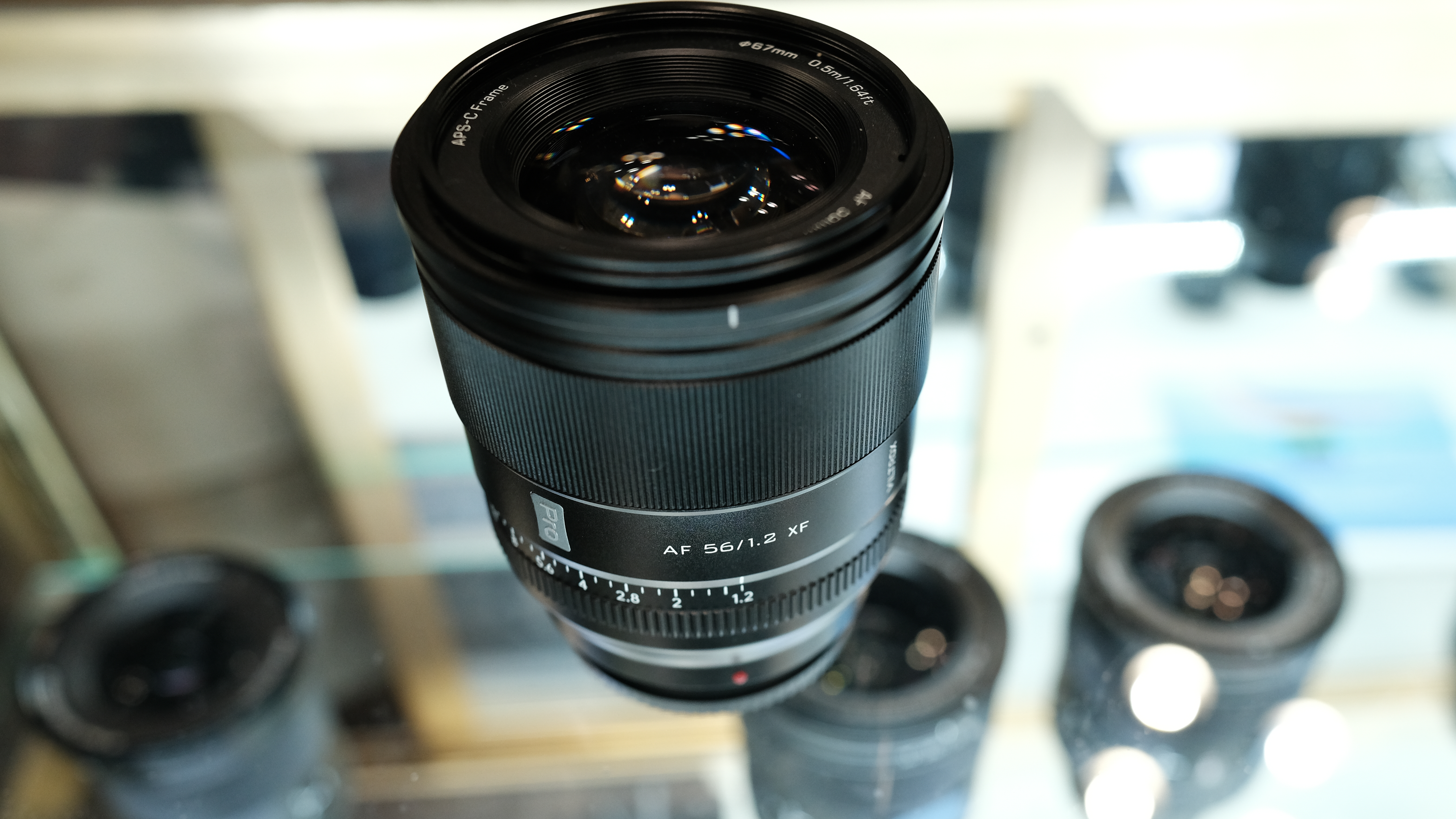The Viltrox AF 56mm f/2 Pro XF prototype lens sitting on a glass display case above other lenses