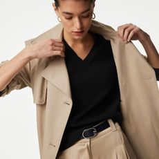 A model wears a black v-neck knit with beige trousers and a beige trench coat