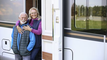 Senior couple camping in a forest with a recreational vehicle (motor home). Both about 65 years old, Caucasian people.