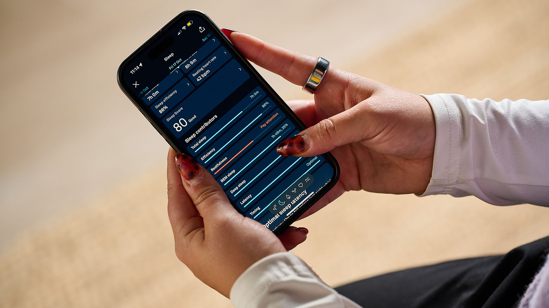 A close up of a pair of hands holding a smartphone. You can see the Oura Ring on the right hand and the phone screen is displaying sleep tracking data