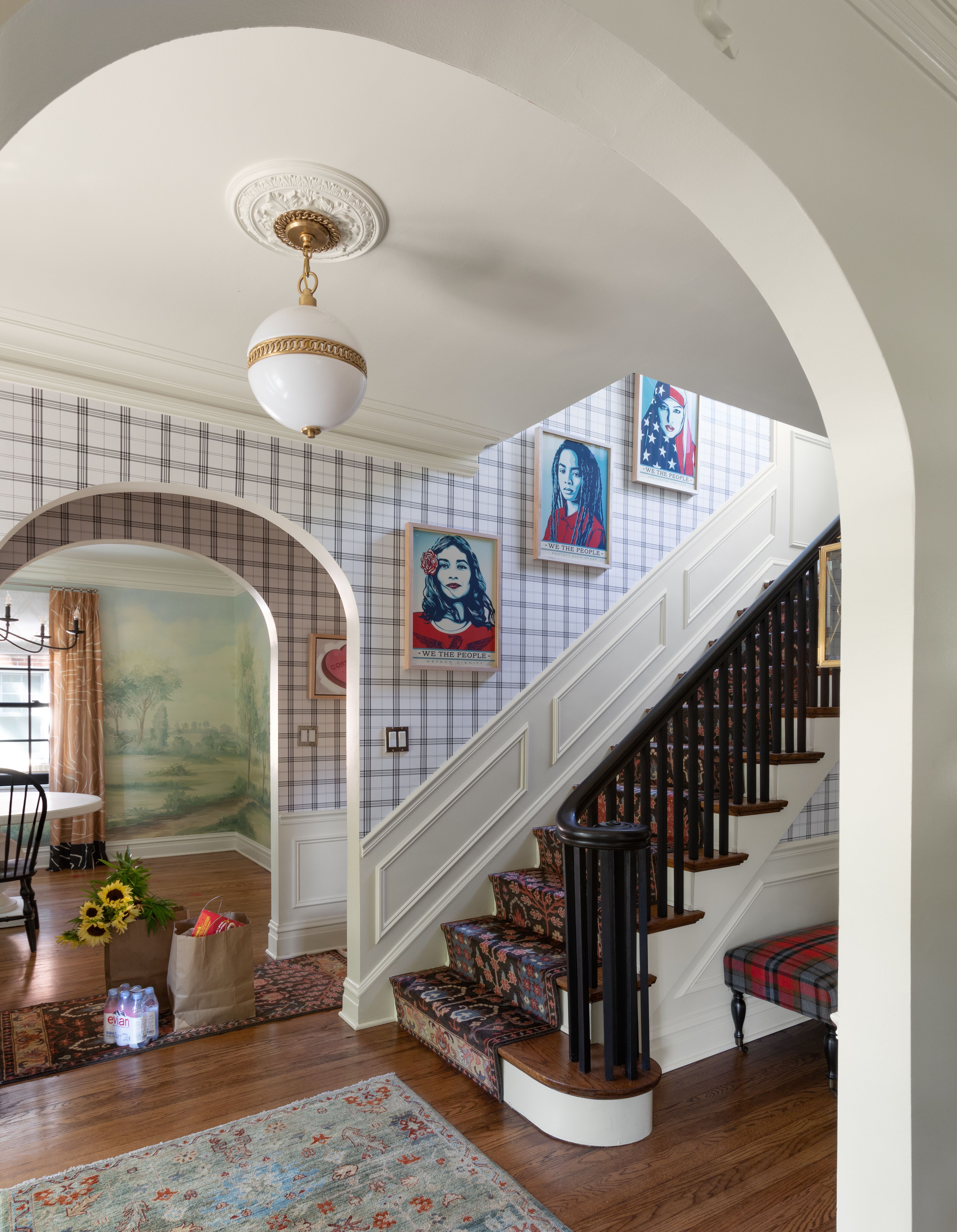 Hallway with wood floor and rug, view to dining room and staircase with plaid wallpaper and artwork