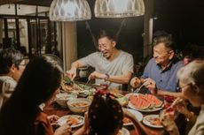 A multigenerational family shares food in a happy mood around a dinner table. 