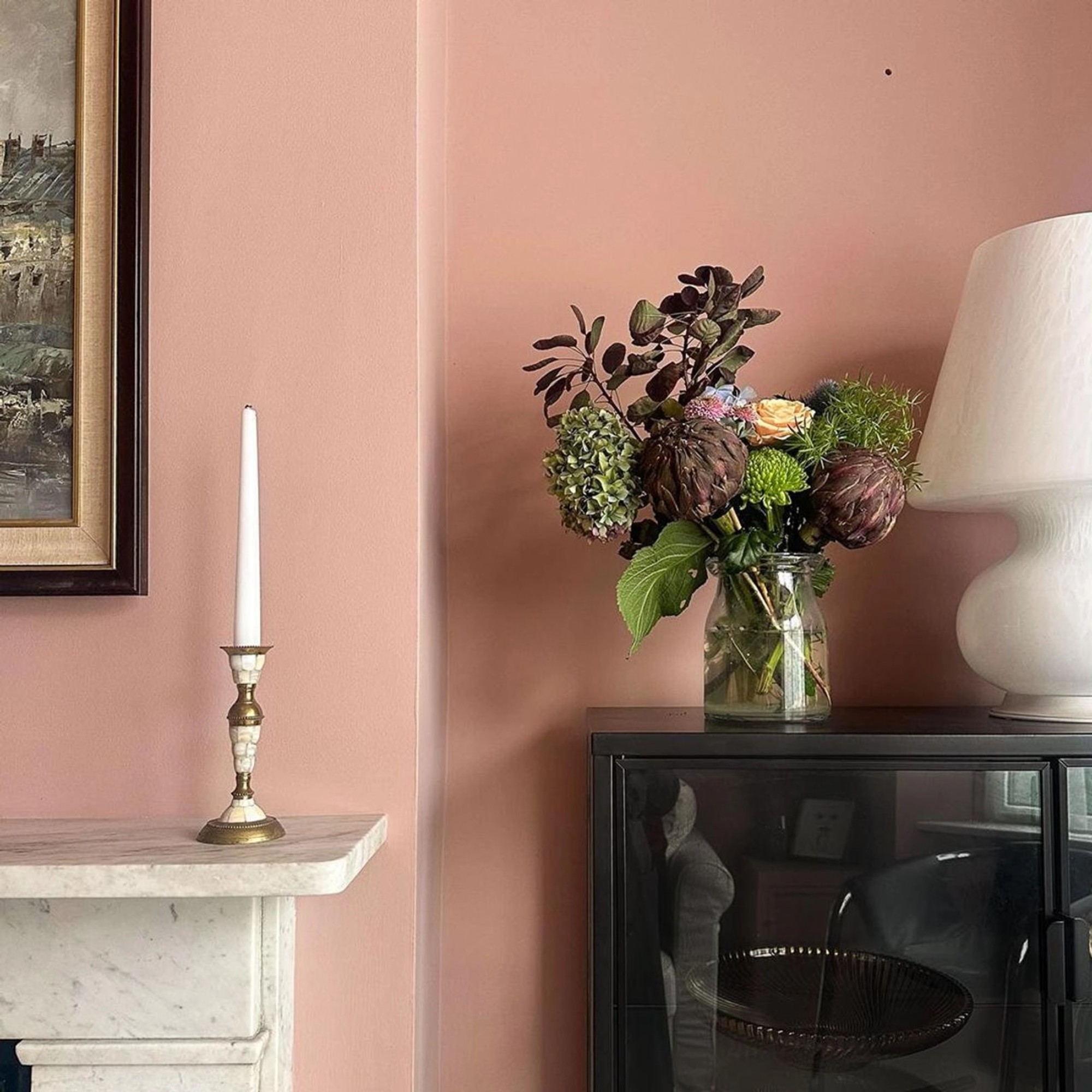 A close-up of a living room painted in Lick's Pink 08 shade with a vase of flowers on a black display cabinet