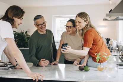 Young woman showing smart phone to brother and parents in the kitchen at home