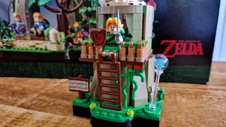 Lego Great Deku Tree Link's house and Young Link minifigure in front of the set box, all on a wooden table