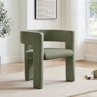 A velvet green chair on a cream rug next to a windwo