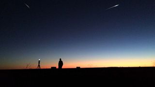 A night scene with the sun falling behind the horizon with two shooting stars lit up in the sky