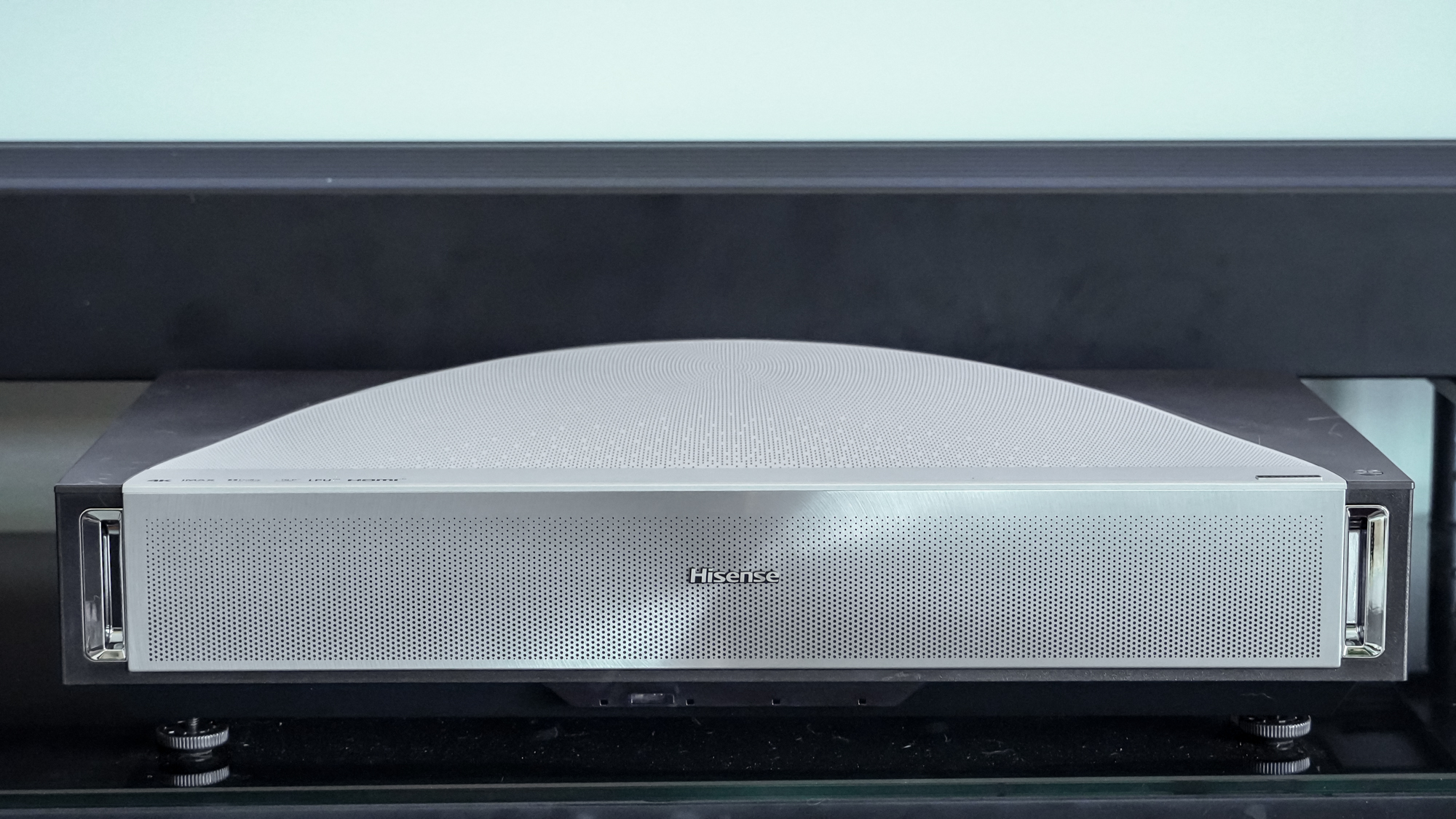 A Hisense PX4 Pro projector on a home media center shelf