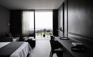 Bedroom with black and white furnishings, a couch, a bed, a chair, and a table on the balcony.