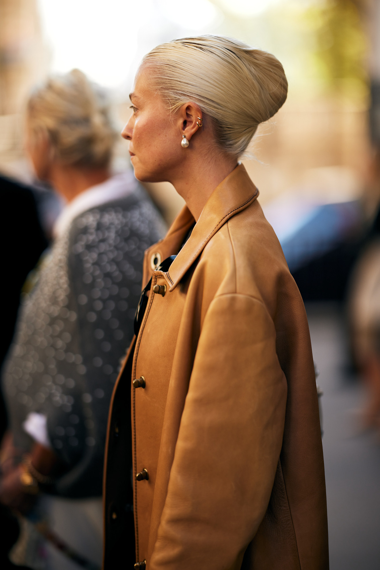 a woman wearing a tan jacket with blonde hair looking away from the camera in a french twist