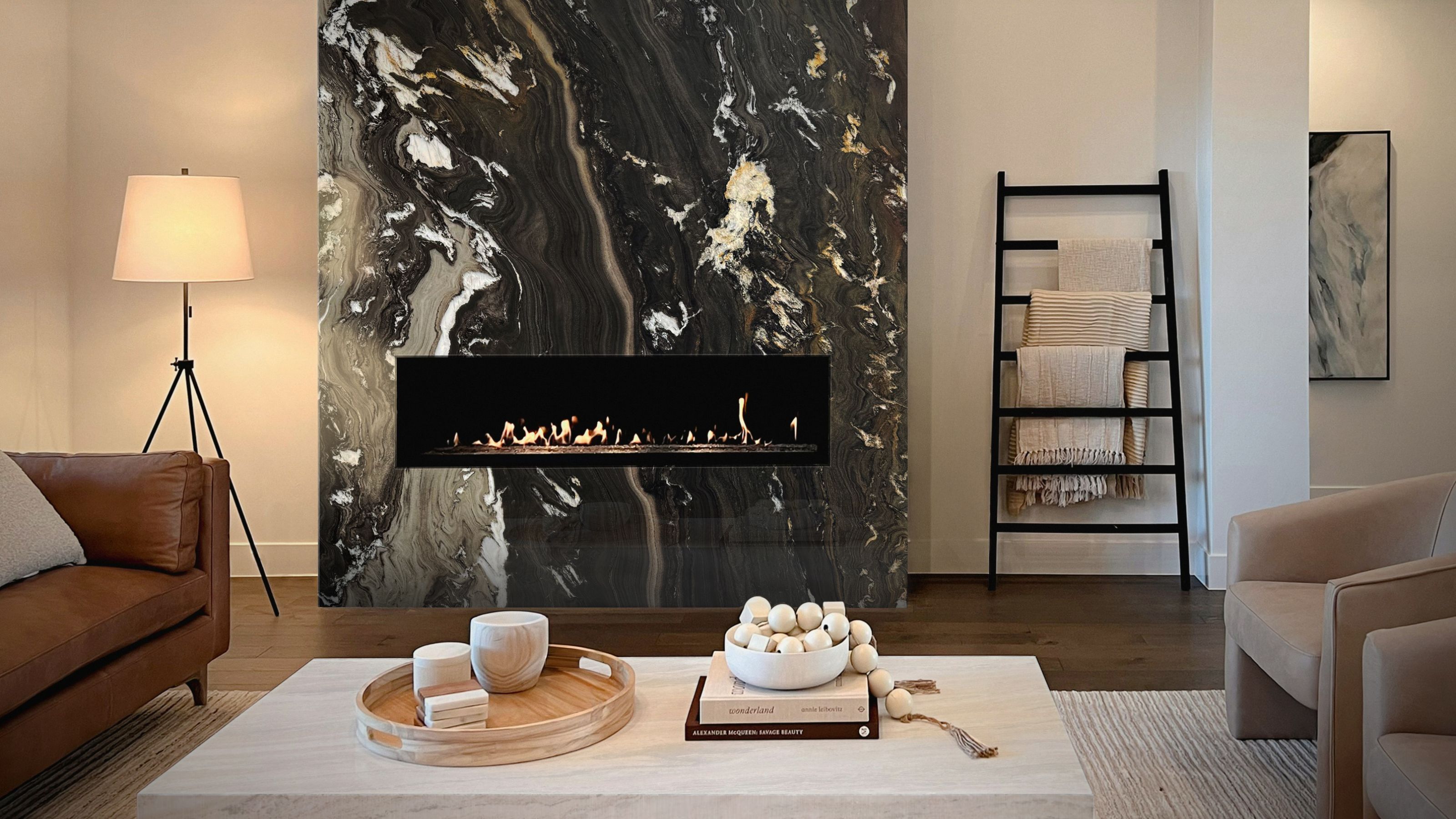 living room with stone fireplace and a towel rail with throws, a floor lamp, tan leather sofa, beige armchairs, and stone coffee table with books and decor