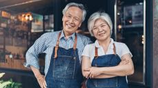 A couple of small business owners in aprons standing in front of their business.