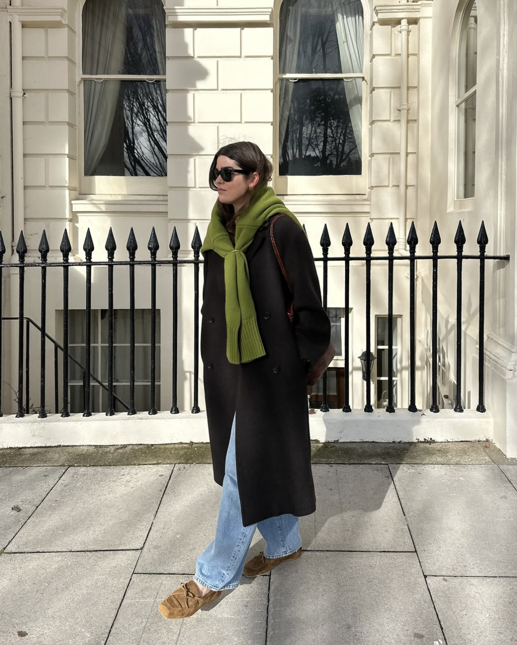 woman in a black coat and jeans with a green sweater tied around her shoulders