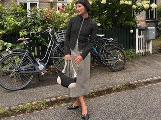 Alyssa wears maxi skirt and black long sleeve top with white and black handbag and black kitten heel shoes surrounded by flowers