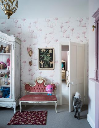 A playroom with pink wallpaper, an armoire and a carved bench