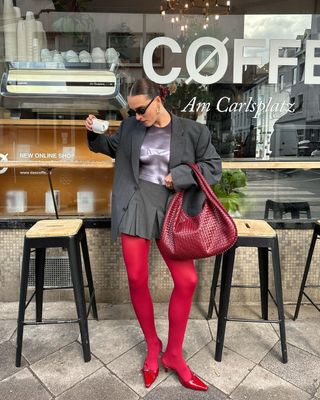 @lara_bsmnn wearing grey blazer, grey skirt, red tights, and red heels