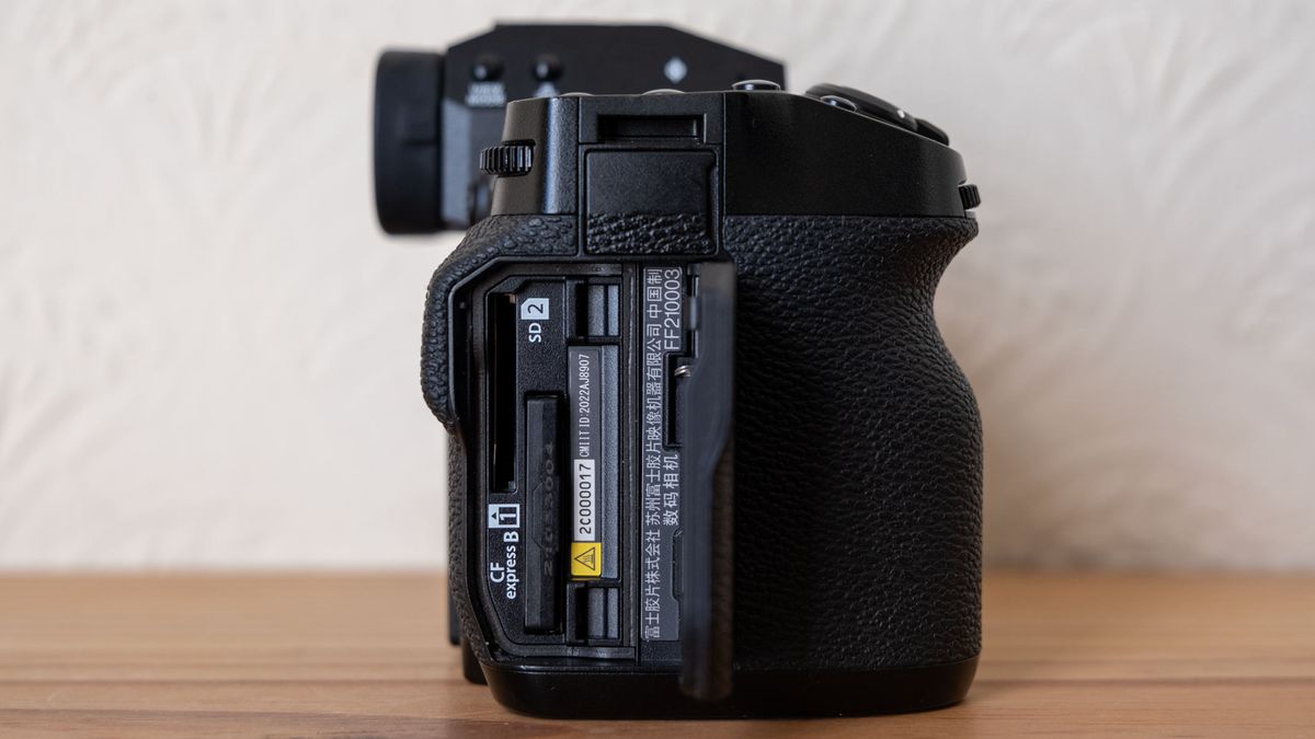 A Fujifilm X-H2 on a wooden shelf with memory card compartment open.