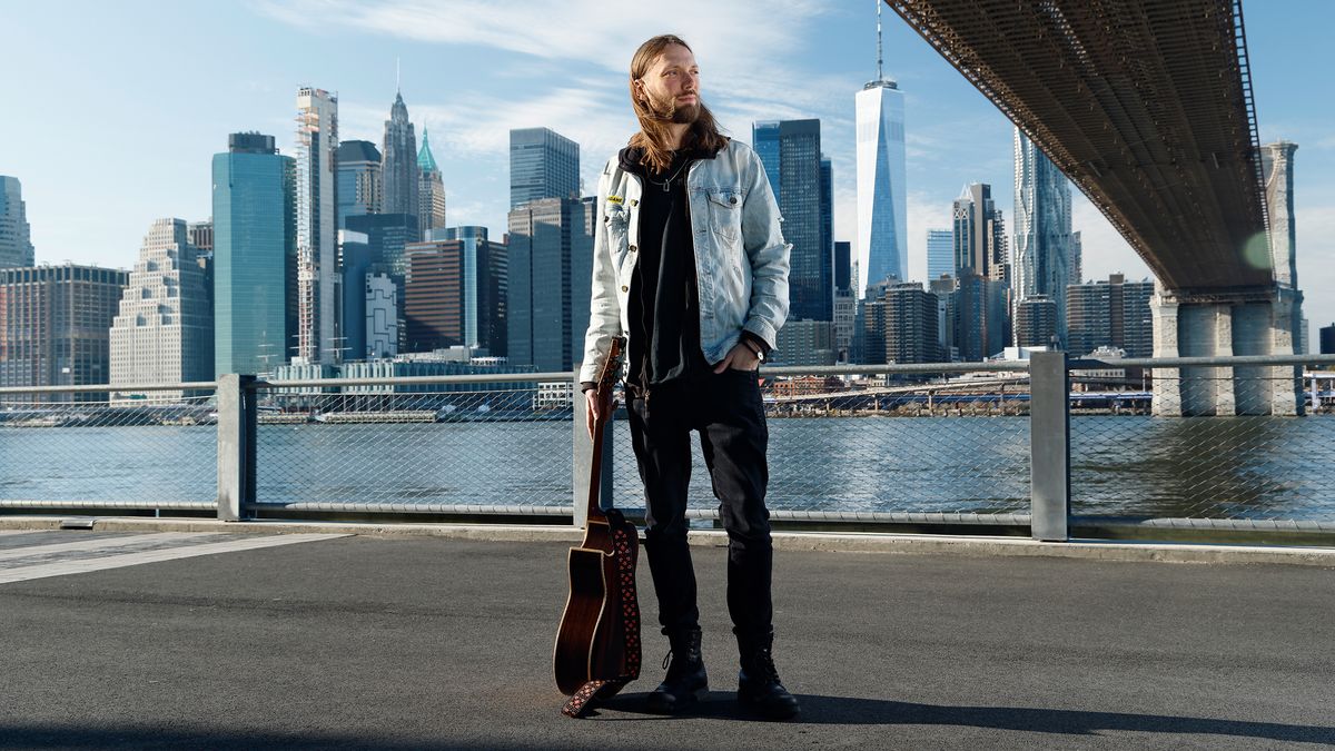 Mike Dawes stands by the Hudson River in New York City with an acoustic guitar