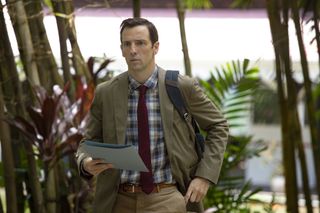 Neville (Ralf Little) stands with his backpack over his shoulder and a blue document folder in his hand, with a determined look on his face