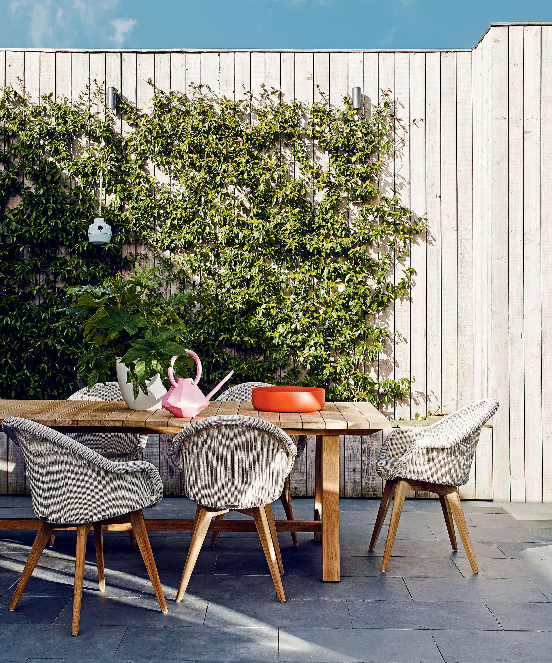 A wooden table and wicker chairs on a patio in the shade.