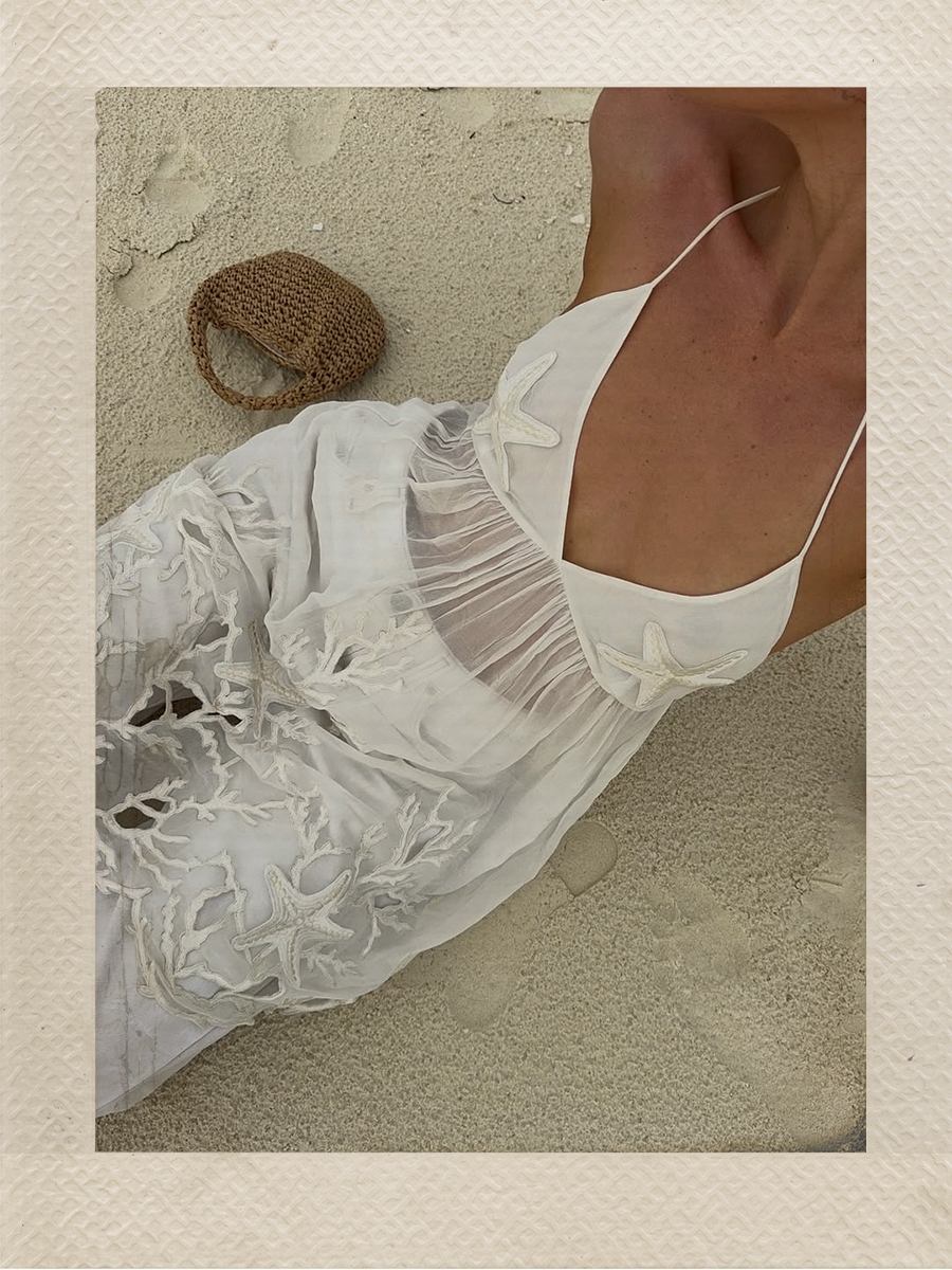 Emma Leger wears a flowing white top with sea star details and white jeans no the beach