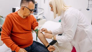 Nurse wiping an older male patient's inner elbow with a cotton swab as she preps for a blood draw