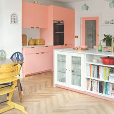 Kitchen with pink cabinets and white island, with herringbone wood flooring on the floor