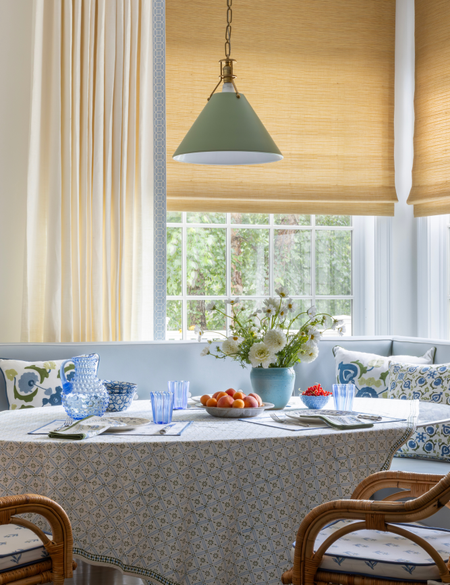 Window area featuring woven bamboo shades layered underneath full-length cream curtains