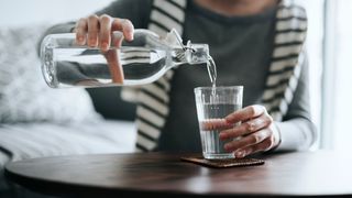 A woman pouring water from a bottle into a glass.