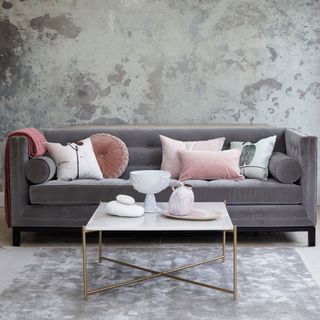 Grey living room with metallic grey wallpaper and a smart grey velvet sofa with pink cushions