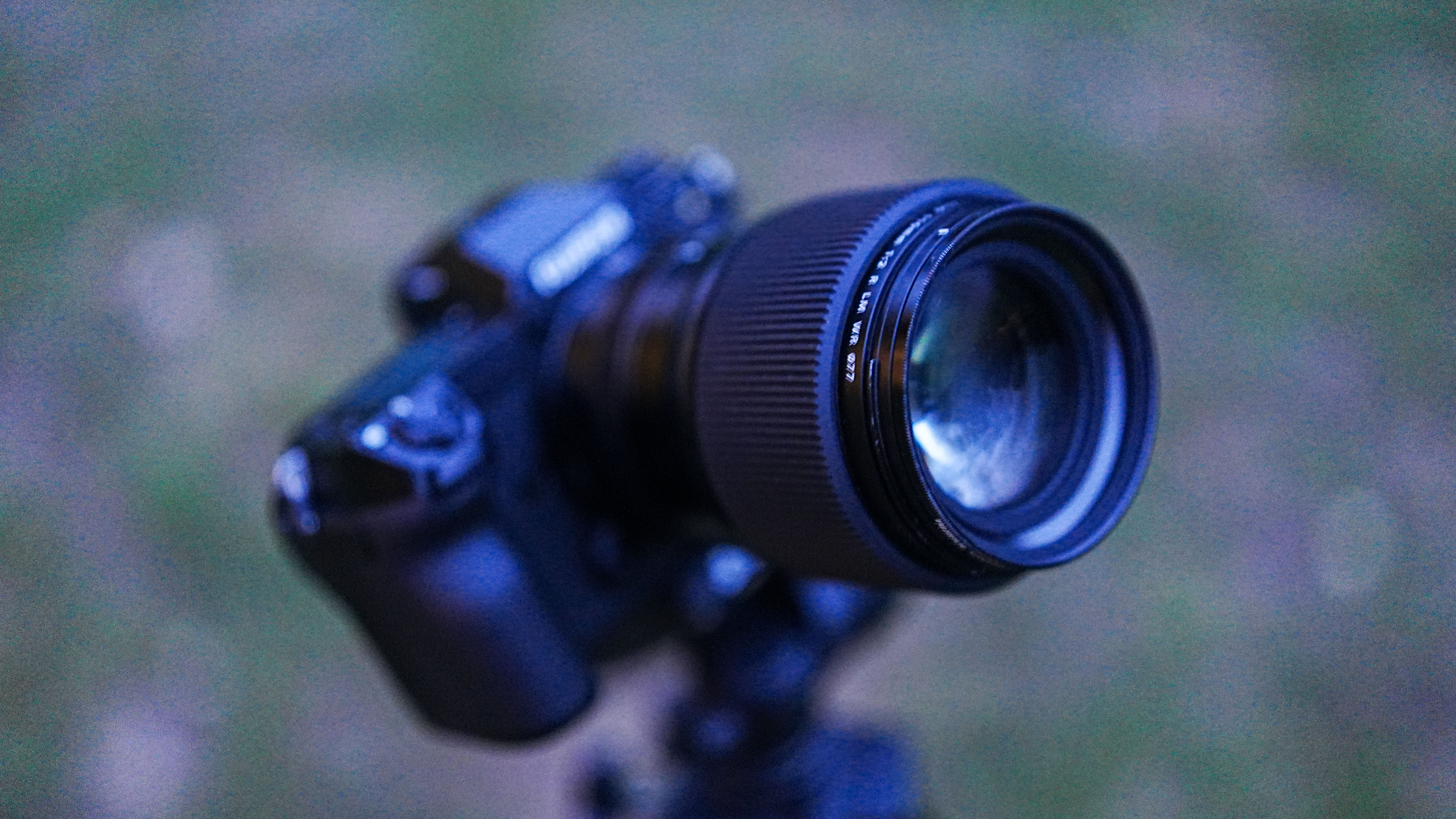 The Fujifilm GFX100S II with the Fujifilm GF 110mm f/2 R WR lens attached, on a tripod, aiming upward, with grass in the background.